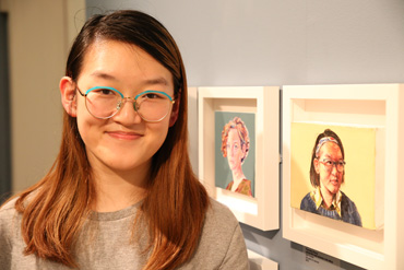 Thumbnail image of Yuanqing Zhang (Leicester High School for Girls student) in front of her prize-winning oil painting,'Self portrait' - Little Selves - Preview Photographs